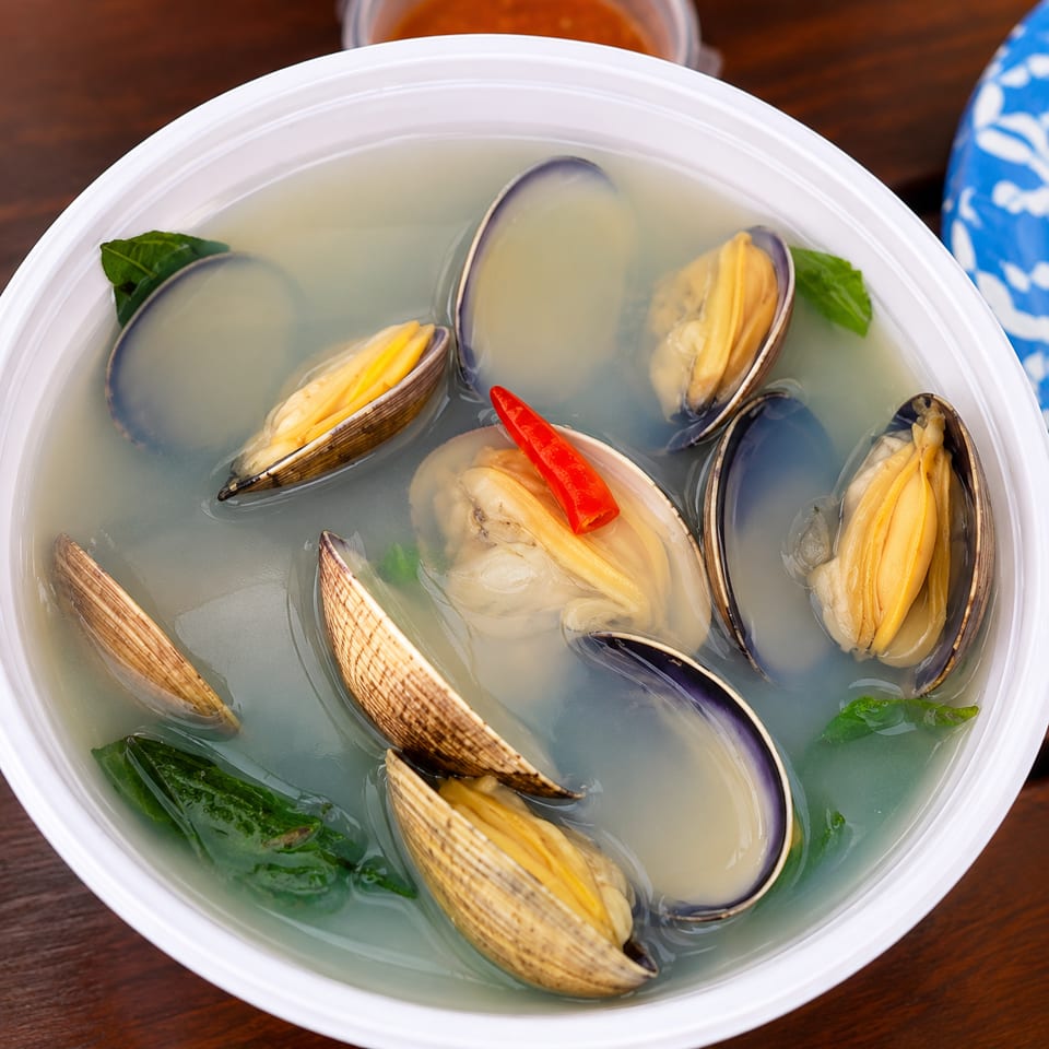 Clam soup with green leaves and a red chili pepper in a white bowl.