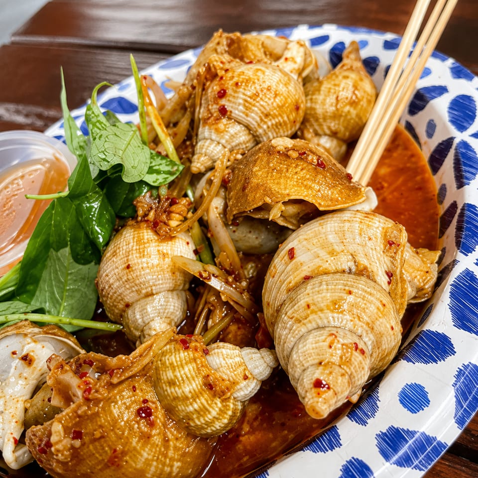 Spicy whelk snails with herbs and sauce in a blue and white patterned bowl.